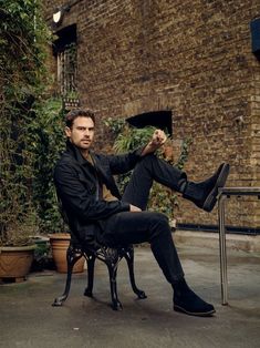 a man sitting in a chair with his legs crossed and wearing black shoes, is posing for the camera