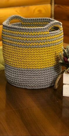 a yellow and grey basket sitting on top of a wooden table next to a white box