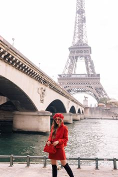 a woman standing in front of the eiffel tower wearing a red coat and black boots