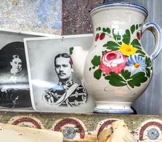 two vases with flowers painted on them are sitting next to other pictures and frames