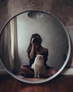 a woman sitting on the floor in front of a mirror with a cat looking at her reflection