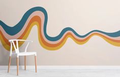 a white chair sitting in front of a wall with an abstract design painted on it