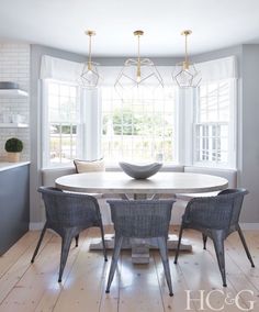 a dining room table with four chairs and a bowl on top of it in front of two windows