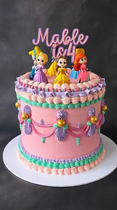 a pink birthday cake decorated with princess characters and the number one on top is made out of fondant