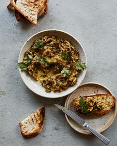 a white bowl filled with food next to slices of bread on top of a table