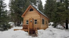 a small wooden cabin in the middle of some snow covered ground with trees around it