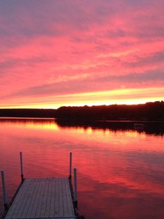 a dock sitting on top of a body of water under a pink sky at sunset