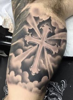 a man's arm with a cross tattoo on it and clouds in the background