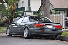 a grey car parked on the side of the road next to a tree and house