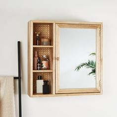 a wooden medicine cabinet sitting next to a mirror on a wall above a towel rack