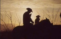 a man riding on the back of a horse next to a dog in front of a sunset