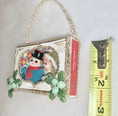 an ornament hanging from a chain next to a measuring ruler with a picture on it