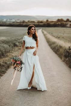 a woman in a white dress is walking down the road with her bouquet on her hand