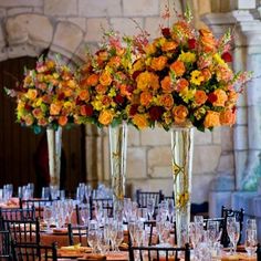 tall vases filled with orange and yellow flowers on top of tables