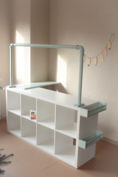 a white shelf sitting in the middle of a room next to a plant and a window