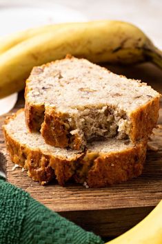 sliced banana bread sitting on top of a wooden cutting board next to two ripe bananas