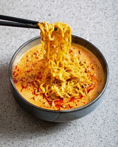 someone is eating noodles with chopsticks in a metal bowl on the floor,