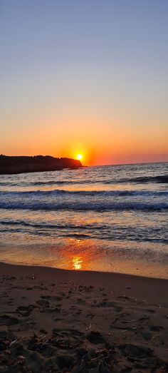 the sun is setting over the ocean with waves coming in from the shore and sand on the beach