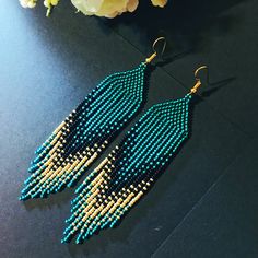 a pair of blue and gold beaded earrings on a table next to some flowers