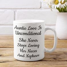 a white coffee mug sitting on top of a wooden table next to a vase with flowers