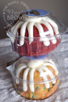 two cupcakes in plastic containers with icing on them