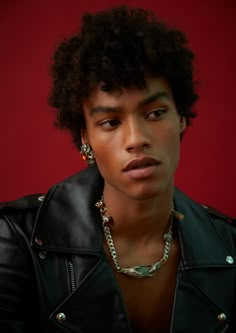 a young man wearing a black leather jacket and chain necklace, looking at the camera