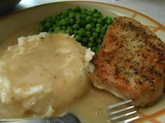 a plate with meat, mashed potatoes and peas on it next to a fork