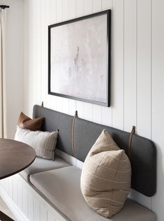 a bench with some pillows on it in front of a wall mounted painting and table