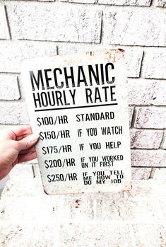 a hand holding up a sign that says mechanic houry rate on the side of a brick wall