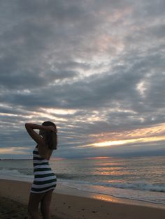 a woman standing on top of a sandy beach next to the ocean under a cloudy sky