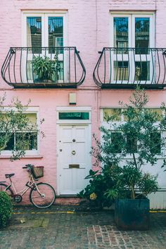 a bicycle parked in front of a pink building with balconies on the windows