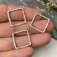 three square shaped silver pendants on a person's hand