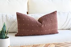 a brown pillow sitting on top of a white couch next to a potted plant