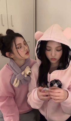 two girls in pink hoodies looking at their cell phones