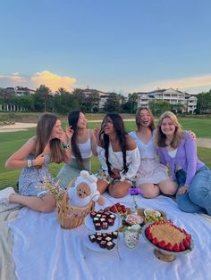 a group of women sitting on top of a white table covered in food and drinks