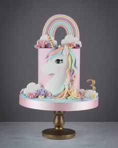 a pink cake with a unicorn's head and rainbows on the top is sitting on a pedestal