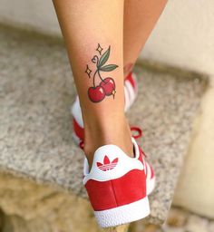 a woman's foot with a cherry tattoo on her left leg and red tennis shoes