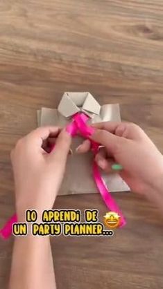 someone is tying the ribbon on top of an origami box with pink tape