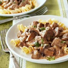 two white plates filled with pasta covered in meat and sauce on top of a green table cloth