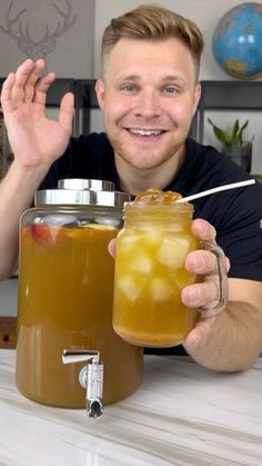 a man sitting at a table with a jar of fruit in front of him and a drink in the other hand