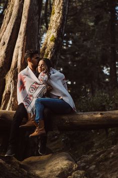 a man and woman sitting on a log in the woods