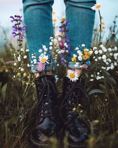 a pair of boots with flowers on them are standing in front of some daisies