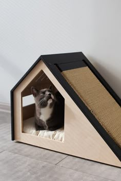 a cat is sitting in a wooden house shaped like a dog house, with the door open