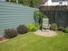 a white chair sitting on top of a lush green field next to a fence and grass covered yard