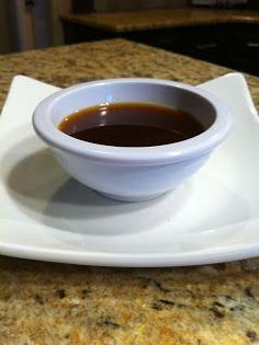 a white bowl filled with sauce on top of a white square plate atop a marble counter