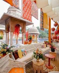 an outdoor seating area with white wicker furniture and colorful flags hanging from the ceiling