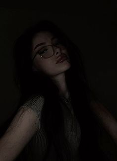 a woman wearing glasses in the dark with her hand on her hip and looking off into the distance