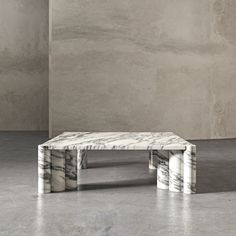 a white marble coffee table sitting on top of a cement floor next to a wall