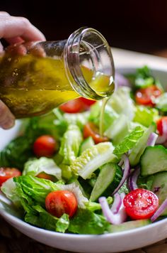 someone pouring dressing into a salad with lettuce, tomatoes and cucumbers