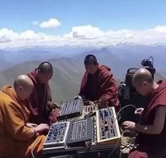 four monks are sitting at a table with electronic equipment in front of them on top of a mountain